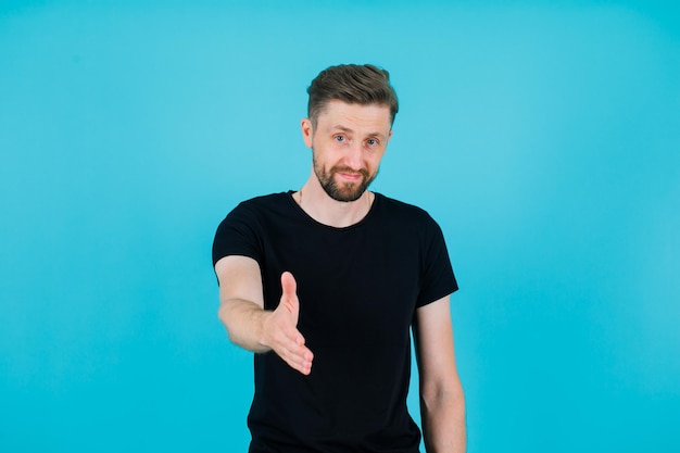 Young man is showing hi gesture by extending hand to camera on blue background