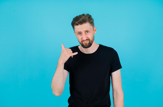 Young man is showing phone gesture with hand on blue background