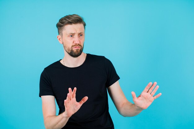 Молодой человек показывает стоп-жест, широко раскрывая горсти на синем фоне