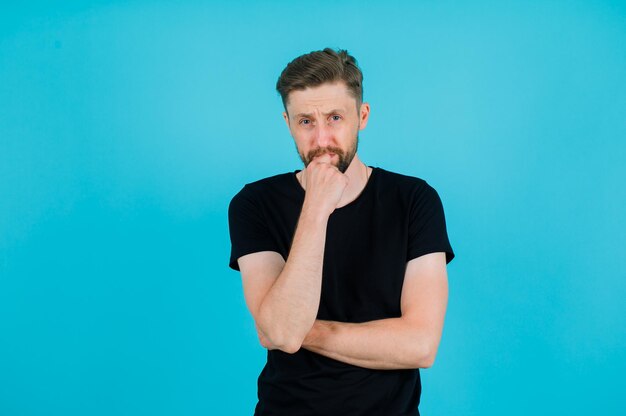 Young man is thinking by putting hand on chin on blue background