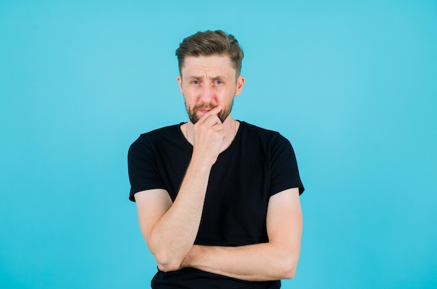 Young man is thinking by putting hand on chin on blue background