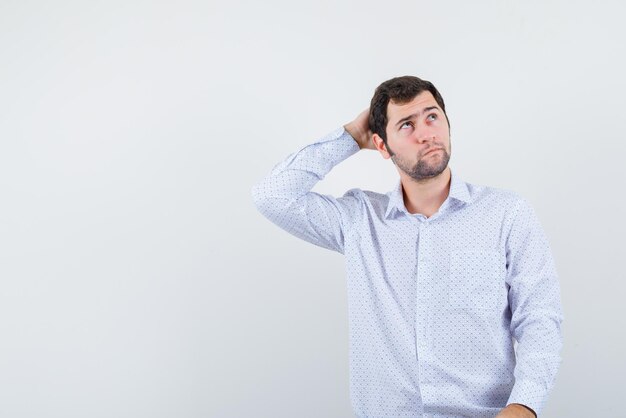 The young man is thinking by putting hand behind head  on white background