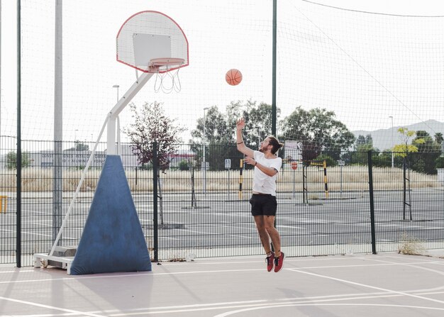 Молодой человек прыгает и бросает баскетбол в обруч