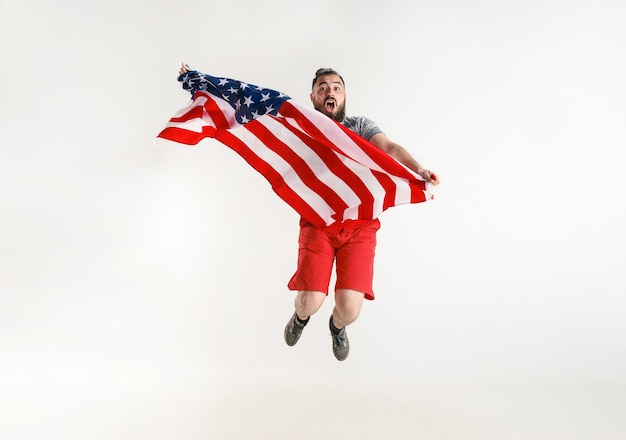 화이트 스튜디오에 고립 된 아메리카 합중국의 국기와 함께 점프하는 젊은 남자.