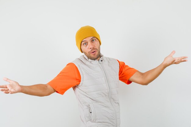 팔을 유지하는 젊은 남자는 t- 셔츠, 재킷, 모자 전면보기에 활짝 열려.