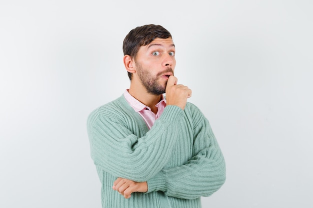 Free photo young man keeping hand on chin in shirt, cardigan and looking wondered. front view.