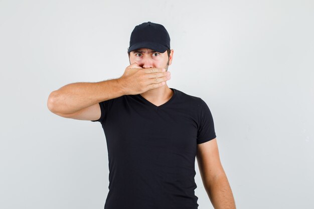 Young man keeping hand on mouth in black t-shirt