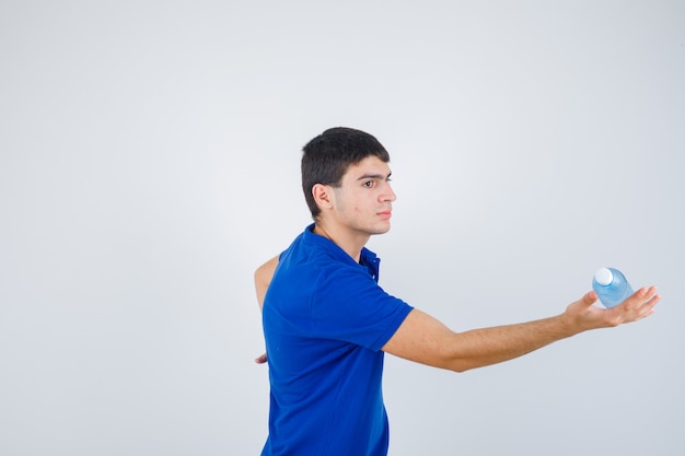 Young man keeping plastic bottle in hand in t-shirt and looking careful .