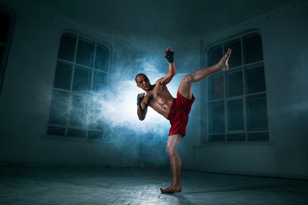 The young man kickboxing in blue smoke