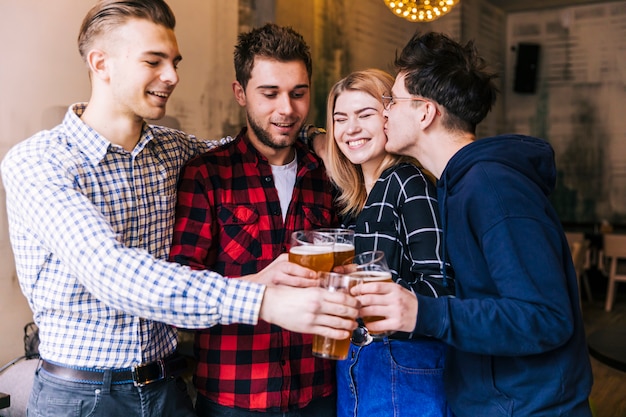 Young man kissing her girlfriend while toasting the beer glasses with friend