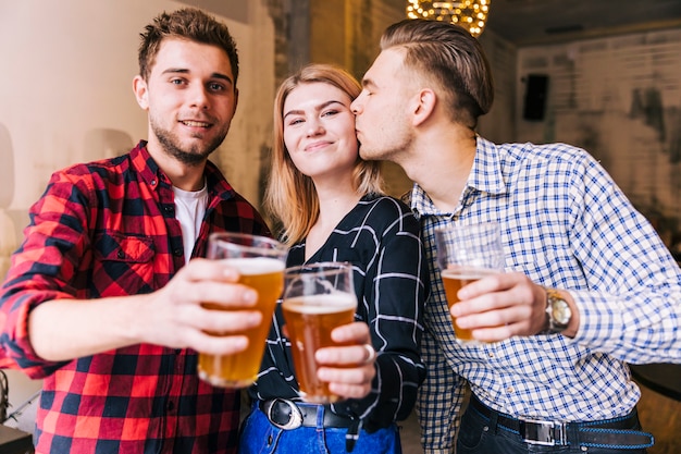 친구와 맥주 잔을 토스트하는 동안 그녀의 여자 친구를 키스하는 젊은 남자