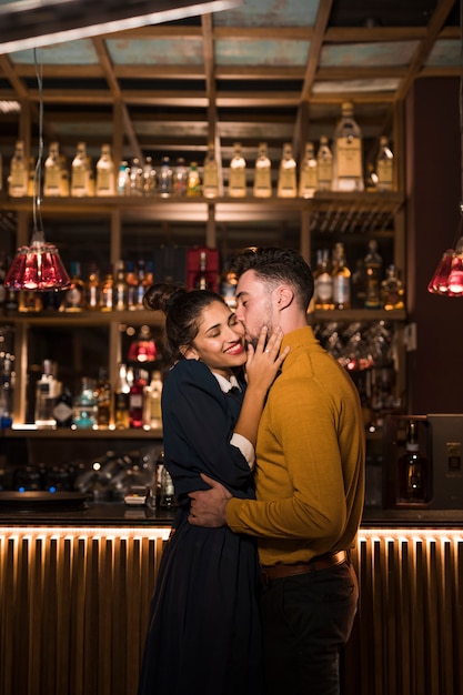 Young man kissing and hugging with positive woman near bar counter