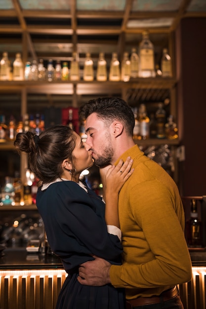 Young man kissing and hugging with woman near bar counter 