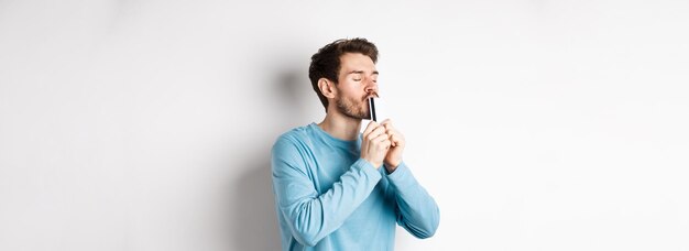 青い cas で白い背景の上に立って満足している顔でプラスチック製のクレジット カードにキスをする若い男