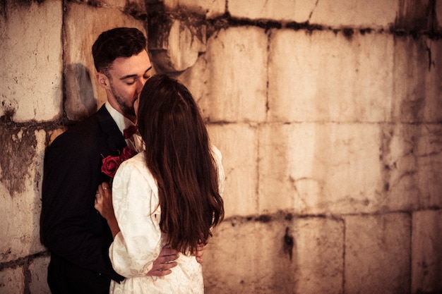 Free photo young man kissing woman leaning on building wall