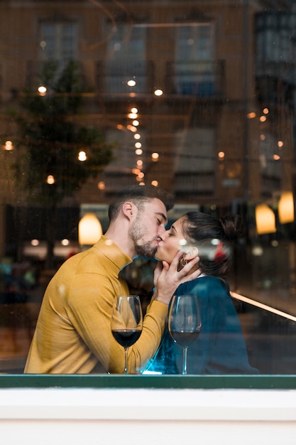 Young man kissing woman near glasses in restaurant