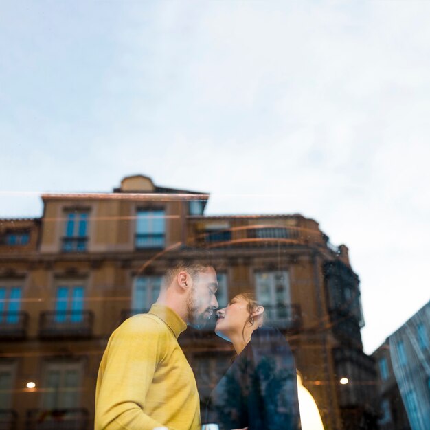 Young man kissing woman other side of window