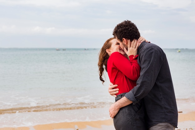 Young man kissing woman on sea shore 