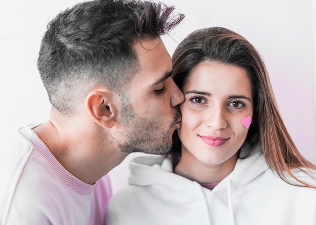 Молодой человек целует женщину с бумажным сердцем на лице
