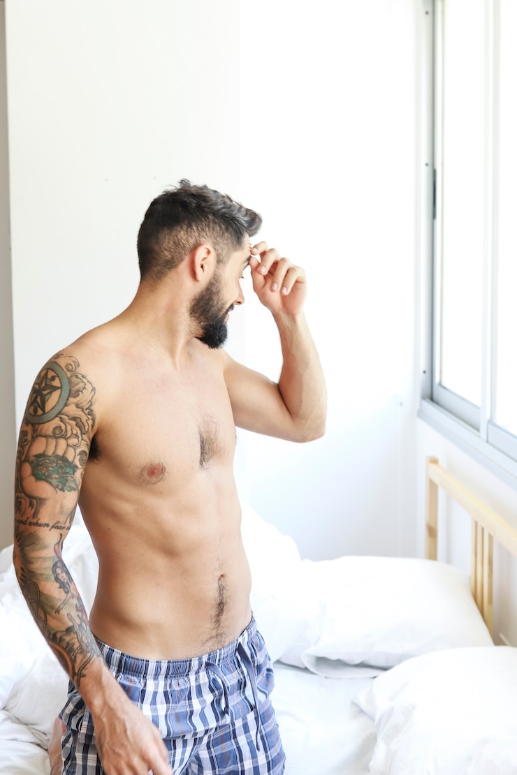 Free Photo young man kneeling on bed at morning