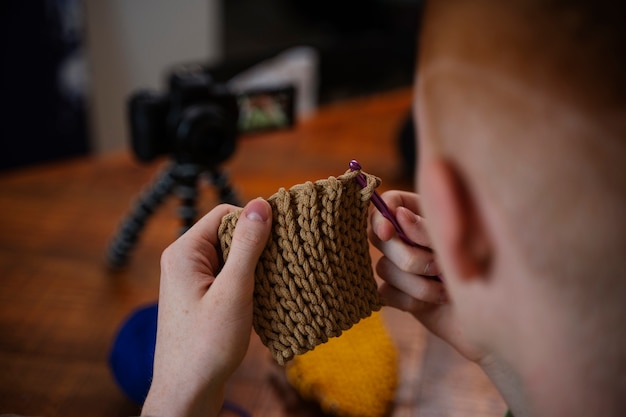 Young man knitting on camera close up