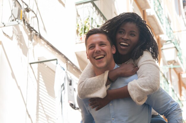 Young man laughing and carrying girlfriend on back outdoors