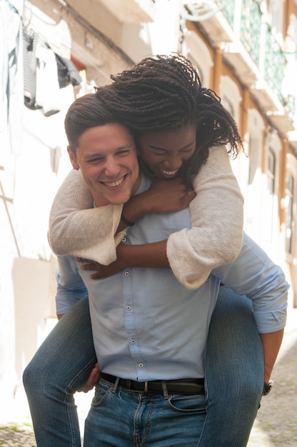 Free photo young man laughing and carrying woman on back outdoors