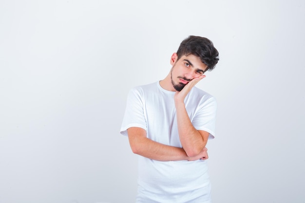 Young man leaning cheek on hand in t-shirt and looking wistful