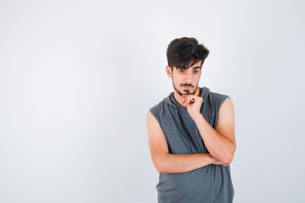 Young man leaning cheek on palm in gray t-shirt and looking pensive