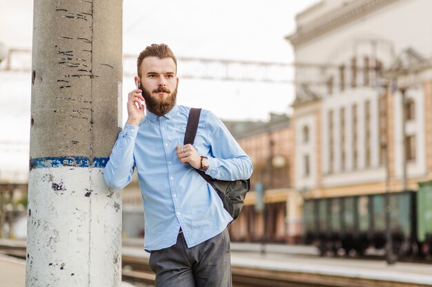 Young man leaning on column talking on cellphone at railway station