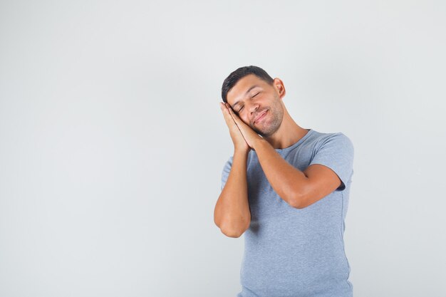 Young man leaning on palms as pillow in grey t-shirt and looking happy