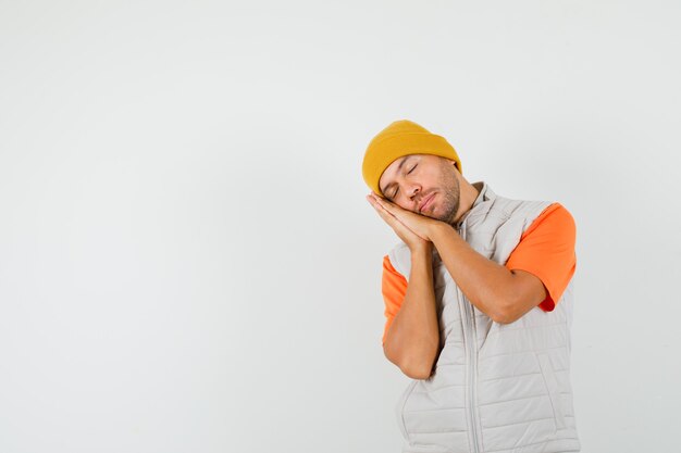 Young man leaning on palms as pillow in t-shirt, jacket, hat and looking relaxed. front view.