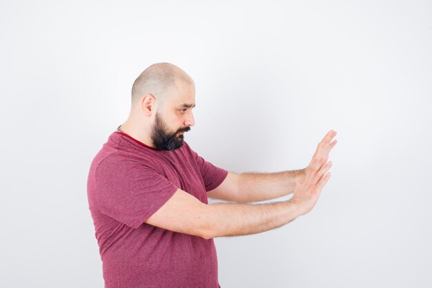 Young man leaning at wall with hands in pink t-shirt .