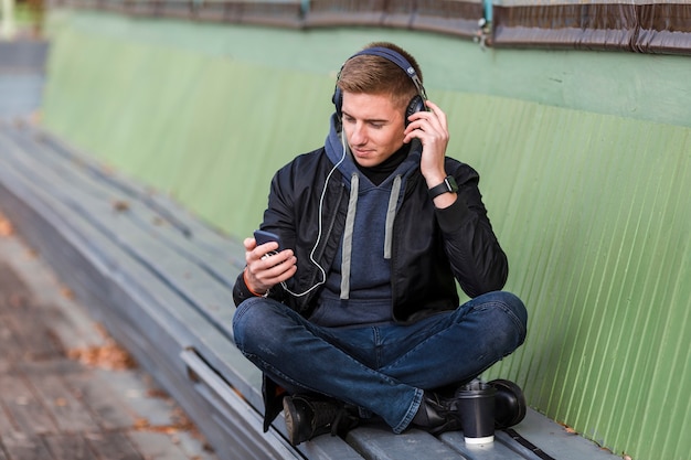 Free photo young man listening to music on headphones on a bench