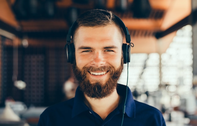 Young man listening music in headphones, using smartphone, outdoor hipster portrait