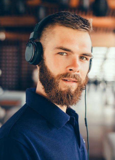 Young man listening music in headphones, using smartphone, outdoor hipster portrait