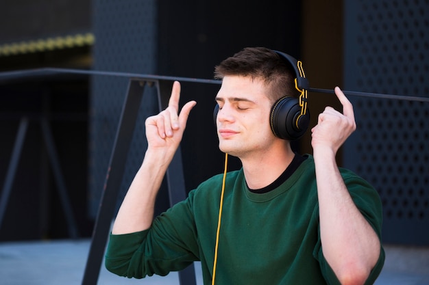 Young man listening to music in headphones with raised hands