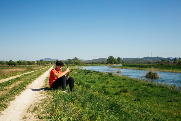 Young man listening music siting in bank of river