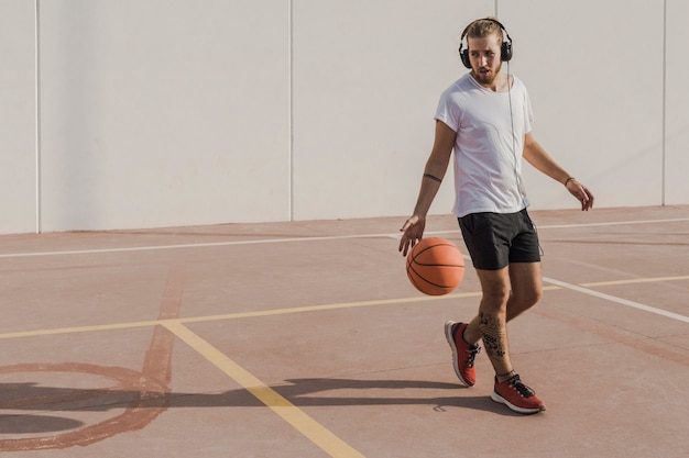 Free photo young man listening to music while playing basketball in court