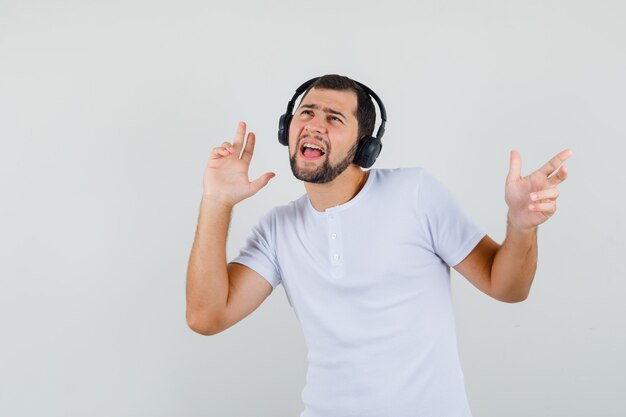 Young man listening music in white t-shirt and looking energetic. front view.