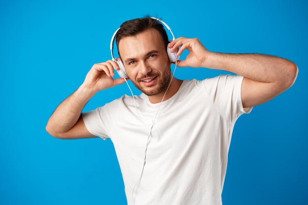 Молодой человек слушает музыку в наушниках на синем фоне