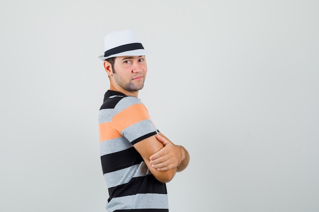 Free photo young man looking aside while crossing his arms in t-shirt,hat and looking calm.