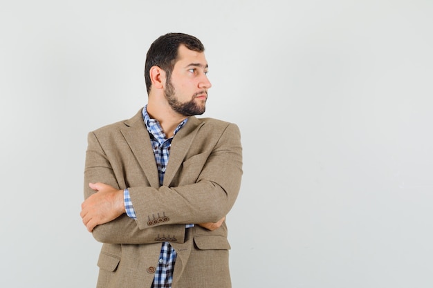 Young man looking aside with crossed arms in shirt, jacket and looking focused. front view.