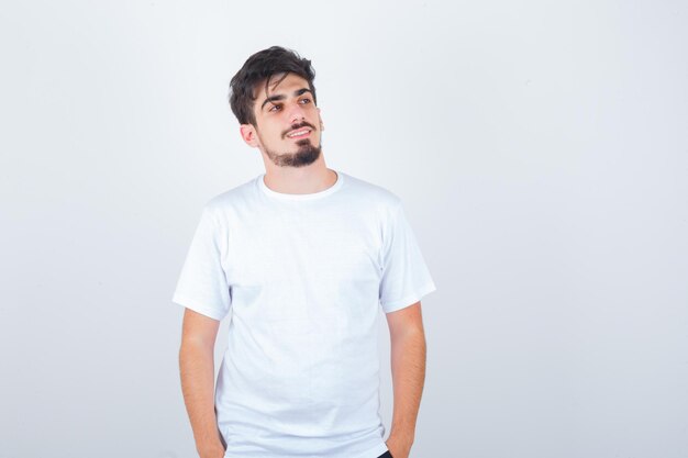 Tシャツに立って、かわいく見えながら目をそらしている若い男