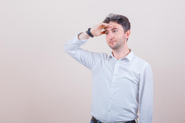 Young man looking away with hand over head in white shirt and looking pensive