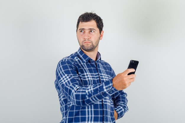 young man looking away with smartphone in his hand in checked shirt and looking displeased