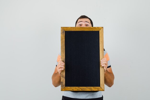 Young man looking over black frame in t-shirt and looking hidden space for text