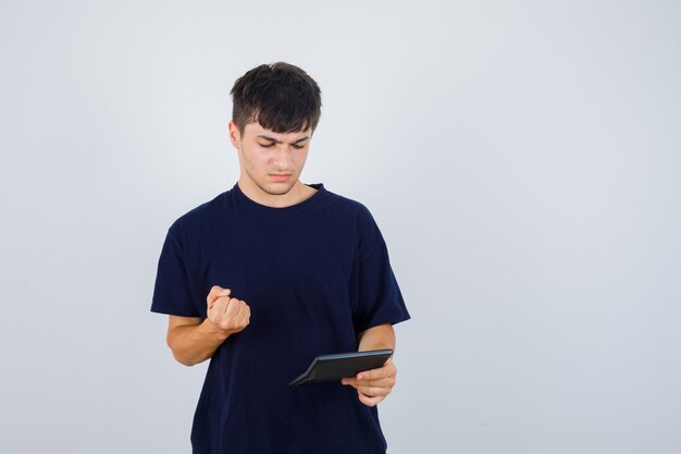 電卓を見て、黒いTシャツで拳を握りしめ、真剣に見える若い男。正面図。
