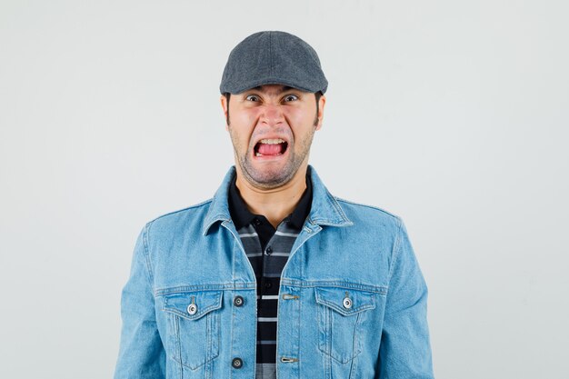 Young man looking at camera in cap, t-shirt, jacket and looking nervous. 