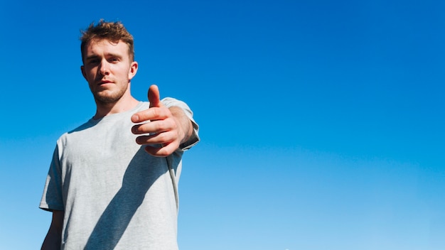 Young man looking at camera and inviting someone against blue sky background